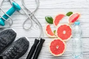 Sport shoes, rope, bottle of water and fresh grapefruits on rustic white wooden table, fitness accessories. Concept of healthy lifestyle, slimming, dieting and healthy nutrition