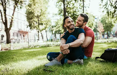 Two Latino men sitting on grass hugging