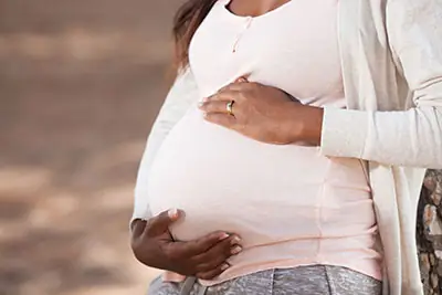 Side view of pregnant woman holding her belly, sitting on the couch, wearing blue shirt
