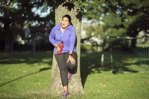 Усталая женщина прислонилась к дереву после тренировки