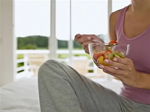 Женщина сидит на кровати, держит фруктовый салат, средняя часть