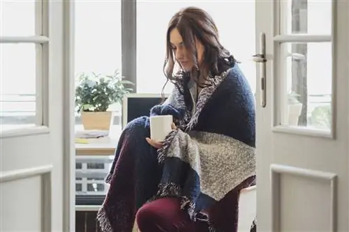 Женщина, завернутая в одеяло, держит кружку