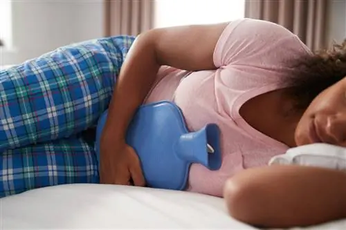 Женщина в пижаме лежит в постели с грелкой от судорог