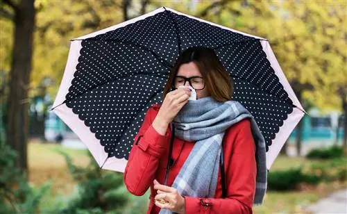 Женщина с зонтиком в горошек прижимает к носу салфетку.