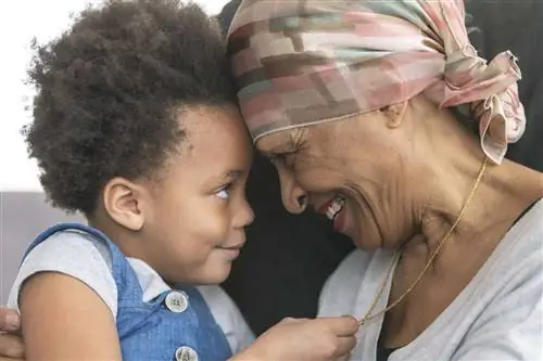 Черная женщина, больная раком, носит платок на голове и улыбается своему маленькому внуку.