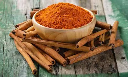 Чаша молотой корицы на деревянном столе с палочками корицы