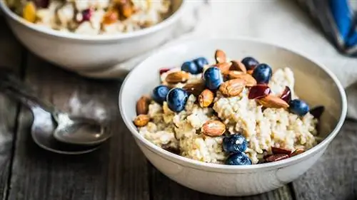 белая миска овсянки с черникой, миндалем и вишней, на столе с ложками