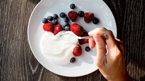 клубника, черника на белой тарелке, сверху женщина ложит йогурт