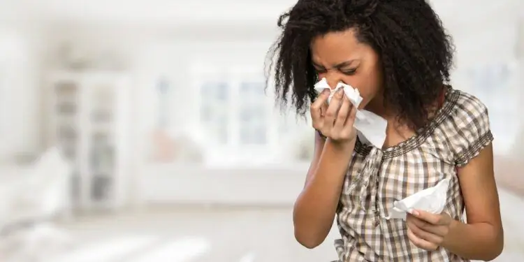 Молодая женщина в клетчатой блузке чихает в носовой платок