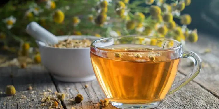 Ромашковый чай, сушеные цветки ромашки в ступке и букет цветков ромашки на деревянном столе