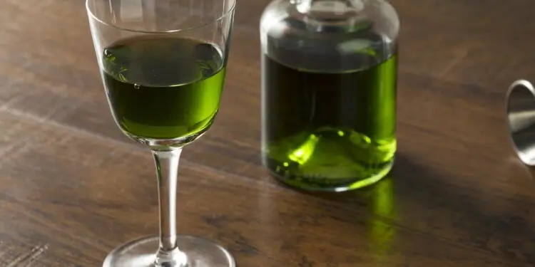 Стеклянный графин и ликерный бокал с абсентом на деревянном столе