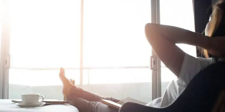Женщина сидит в кресле с кофе и смотрит в окно с поднятыми ногами