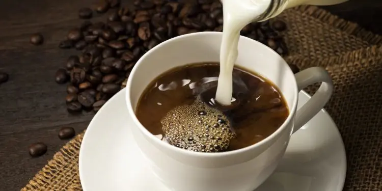 Молоко из стеклянной бутылки наливается в чашку кофе