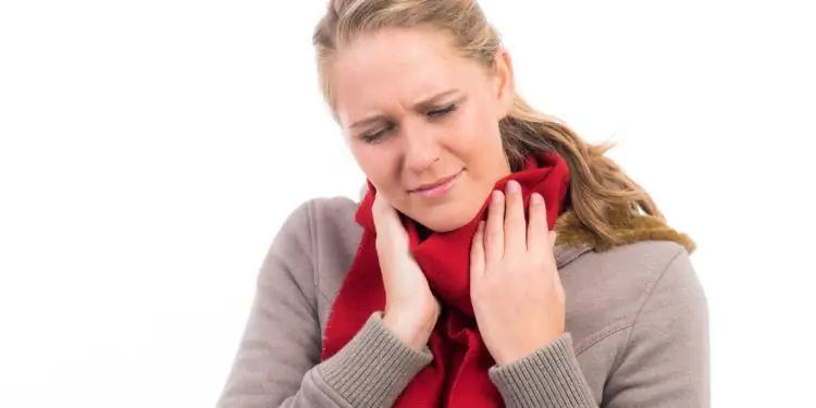 Женщина с болезненным выражением лица и повязанным шарфом прижимает руки к шее