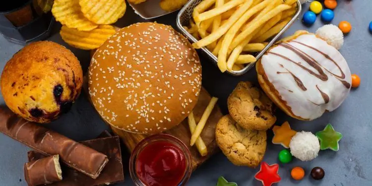 Смесь различных нездоровых продуктов, таких как картофель фри, чипсы, пирожные и сладости