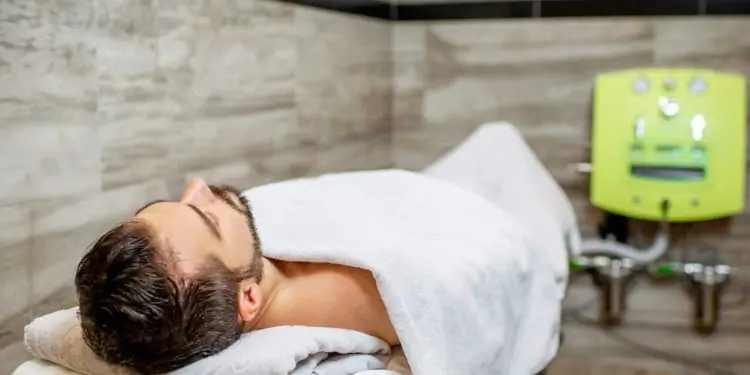 Мужчина лежит на кушетке и подключен к аппарату гидроколонотерапии через трубки