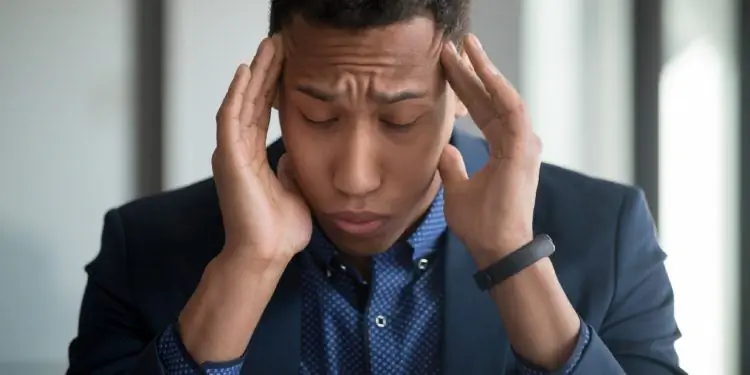 Измученный мужчина сидит перед открытым ноутбуком и держит руки на висках