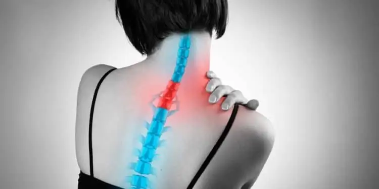 Женщина испытывает боль в шейном отделе позвоночника и прикасается рукой к пораженному участку в верхней части спины